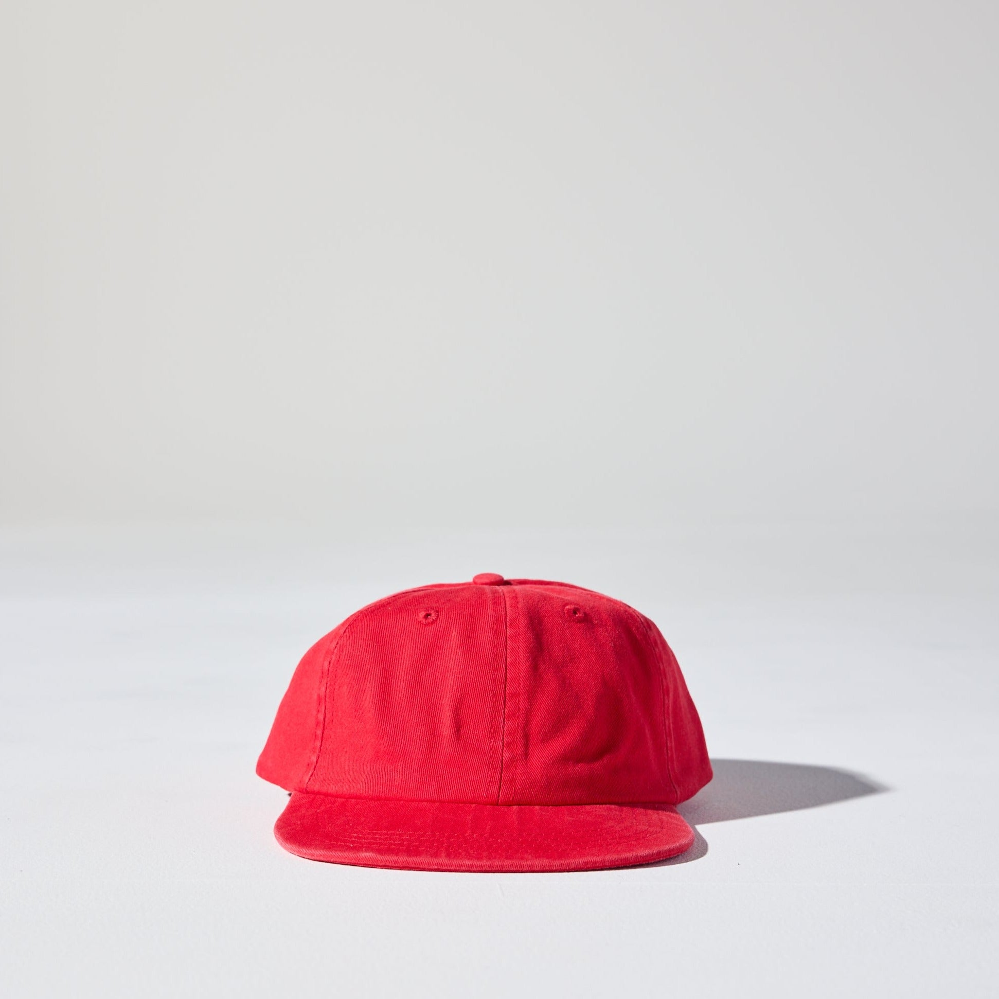 A red 6 panel snapback cap made of recycled cotton twill, displayed against a neutral background. Vintage-style Monday Snap Cap with soft unstructured peak.