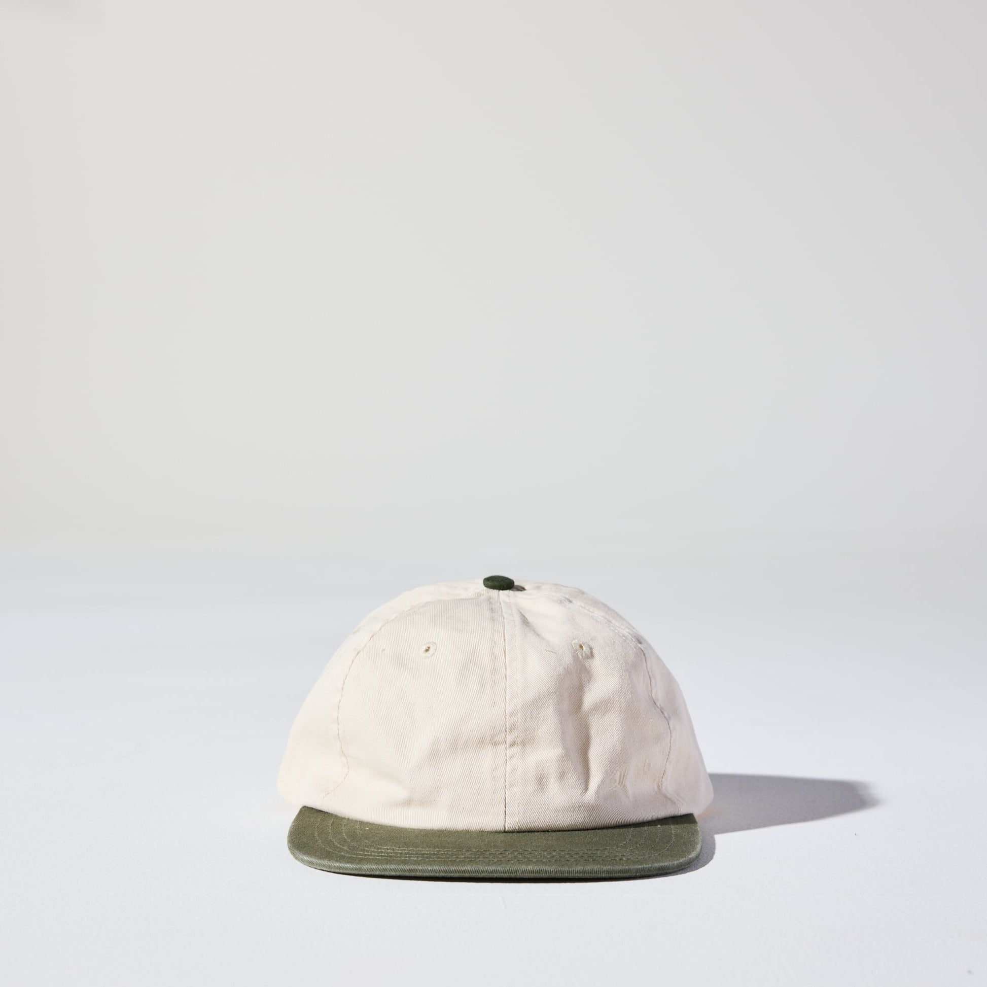 A beige and green two-tone 6 panel hard flat brim cap with an adjustable snap closure. This hat is a 90s Retro low profile Thursday Cap by House of Peaks.