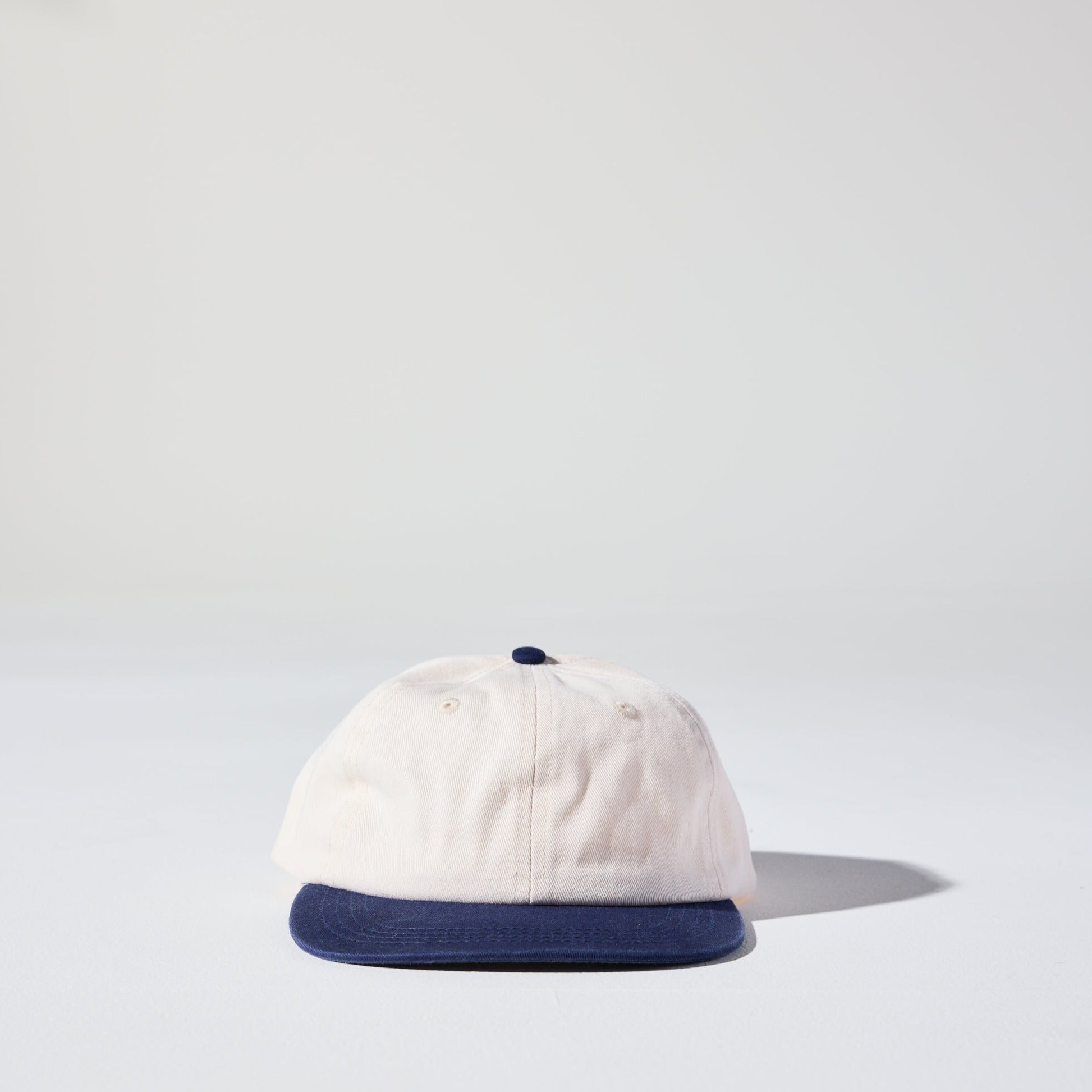 A beige and NAVY two-tone 6 panel hard flat brim cap with an adjustable snap closure. This hat is a 90s Retro low profile Thursday Cap by House of Peaks.