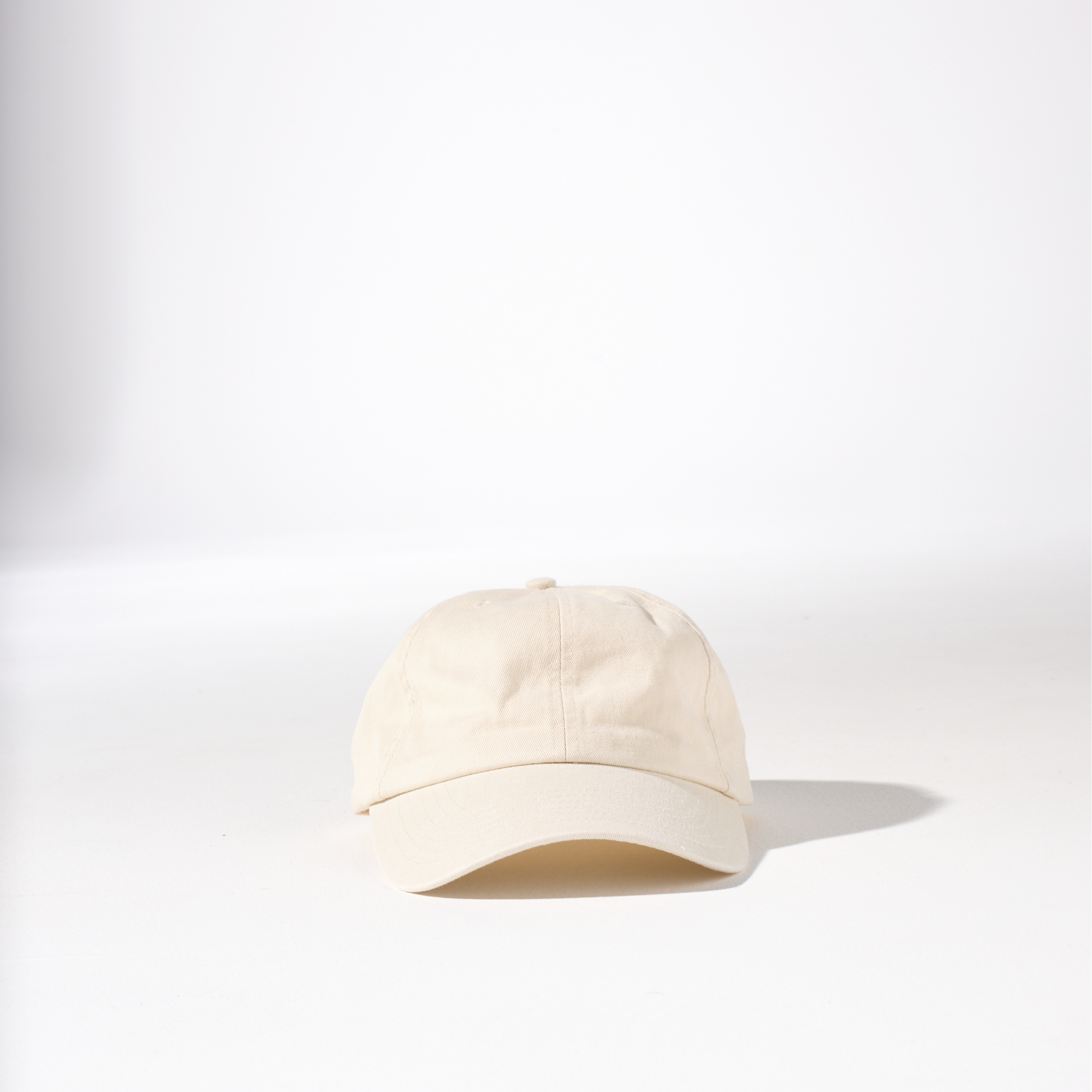 A beige cream-coloured, 6-panel unstructured 'Dad' cap made of recycled cotton twill with an adjustable material buckle. Best Blank Hats by House of Peaks.