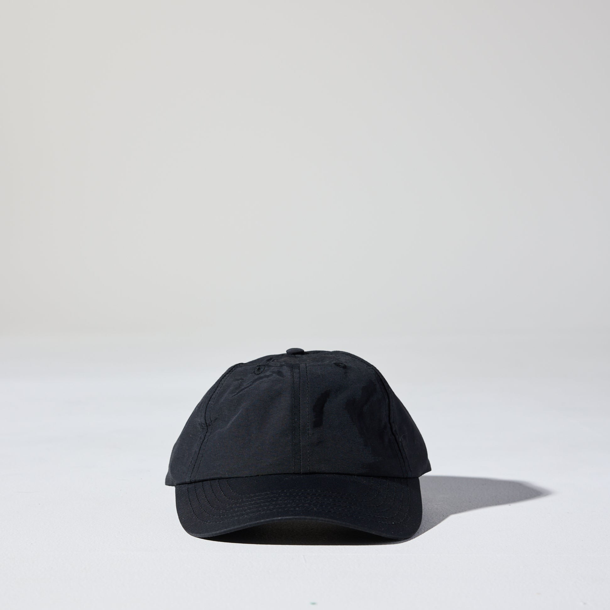 A black lightweight, unstructured nylon running cap, featuring a curved peak and an adjustable strap, placed against a white background.