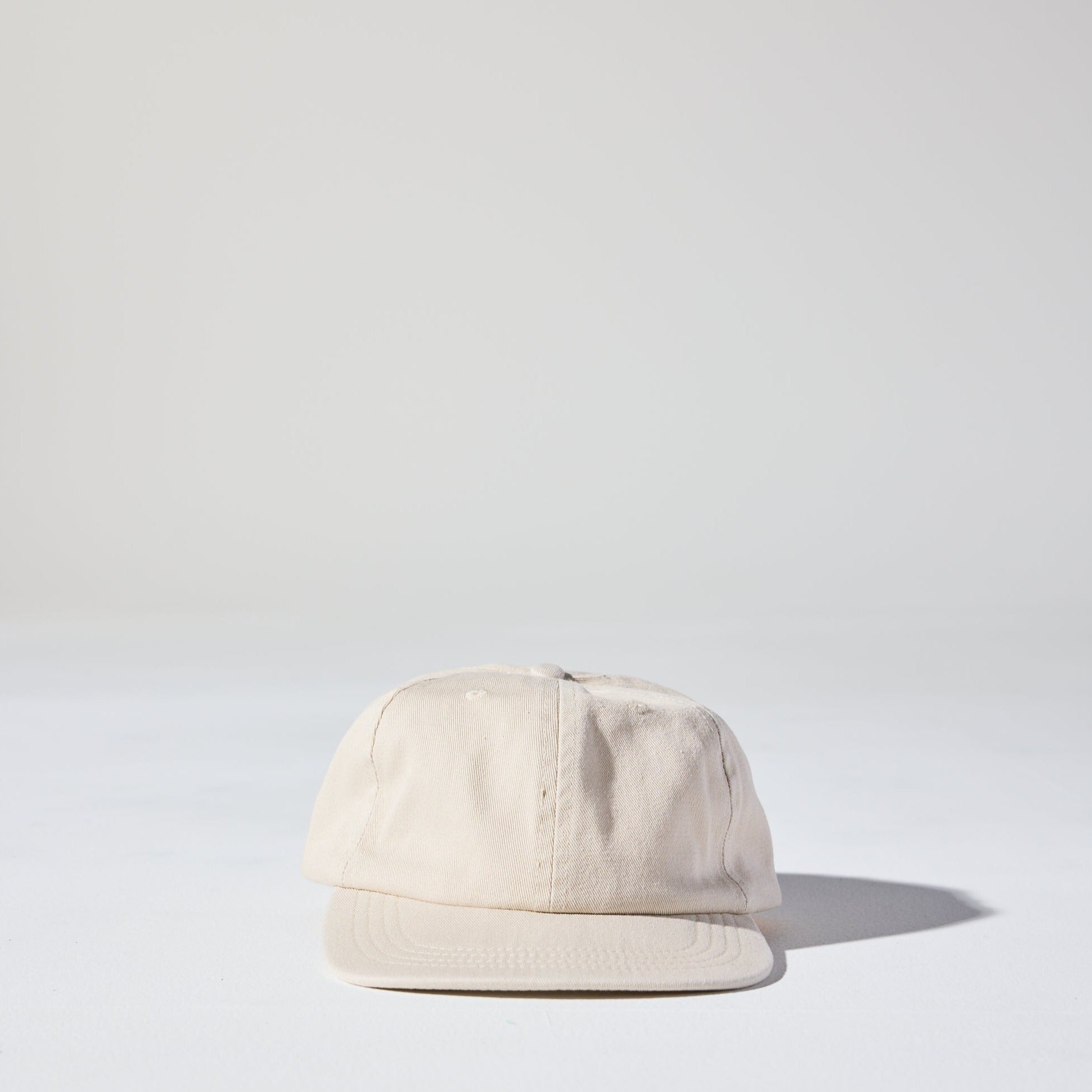 A retro style beige Monday Buckle Cap by House of Peaks with an adjustable strap, placed against a white background.