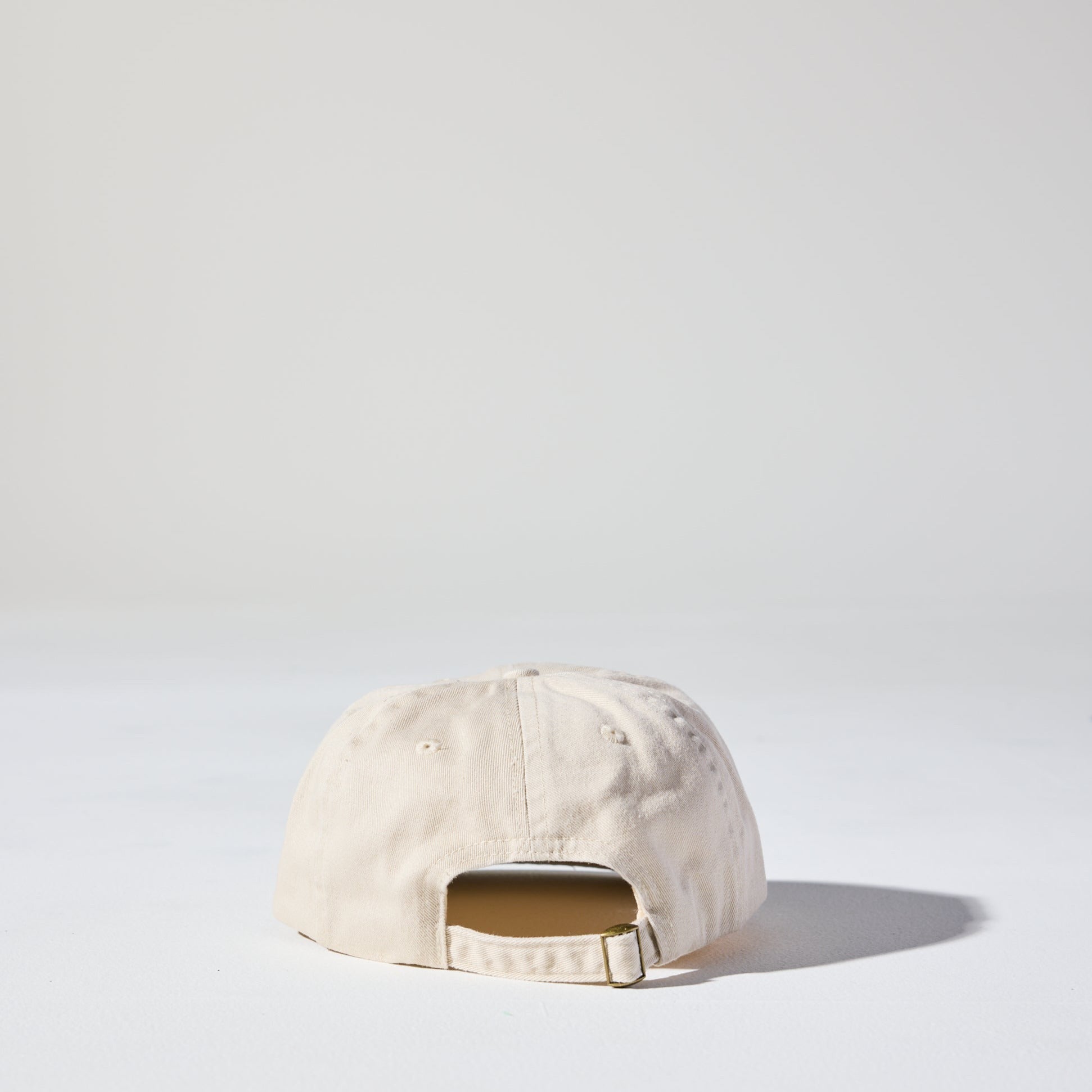 A retro style beige Monday Buckle Cap by House of Peaks with an adjustable strap, placed against a white background.