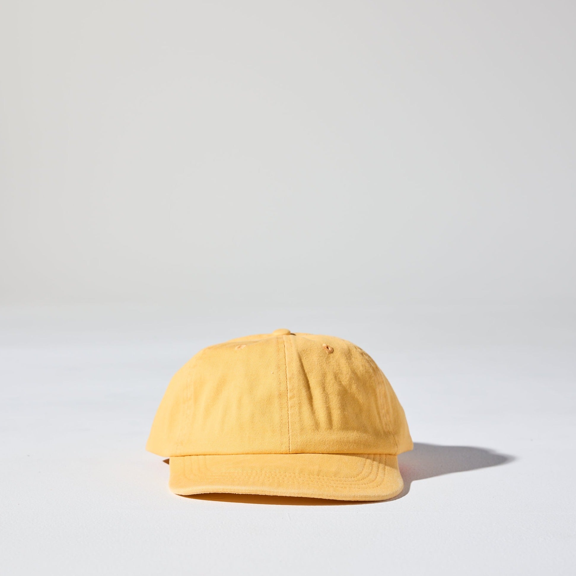 A faded yellow 6 panel snapback cap made of recycled cotton twill, Vintage, worn in style Monday Snap Cap with soft unstructured peak, suitable for adults and kids.