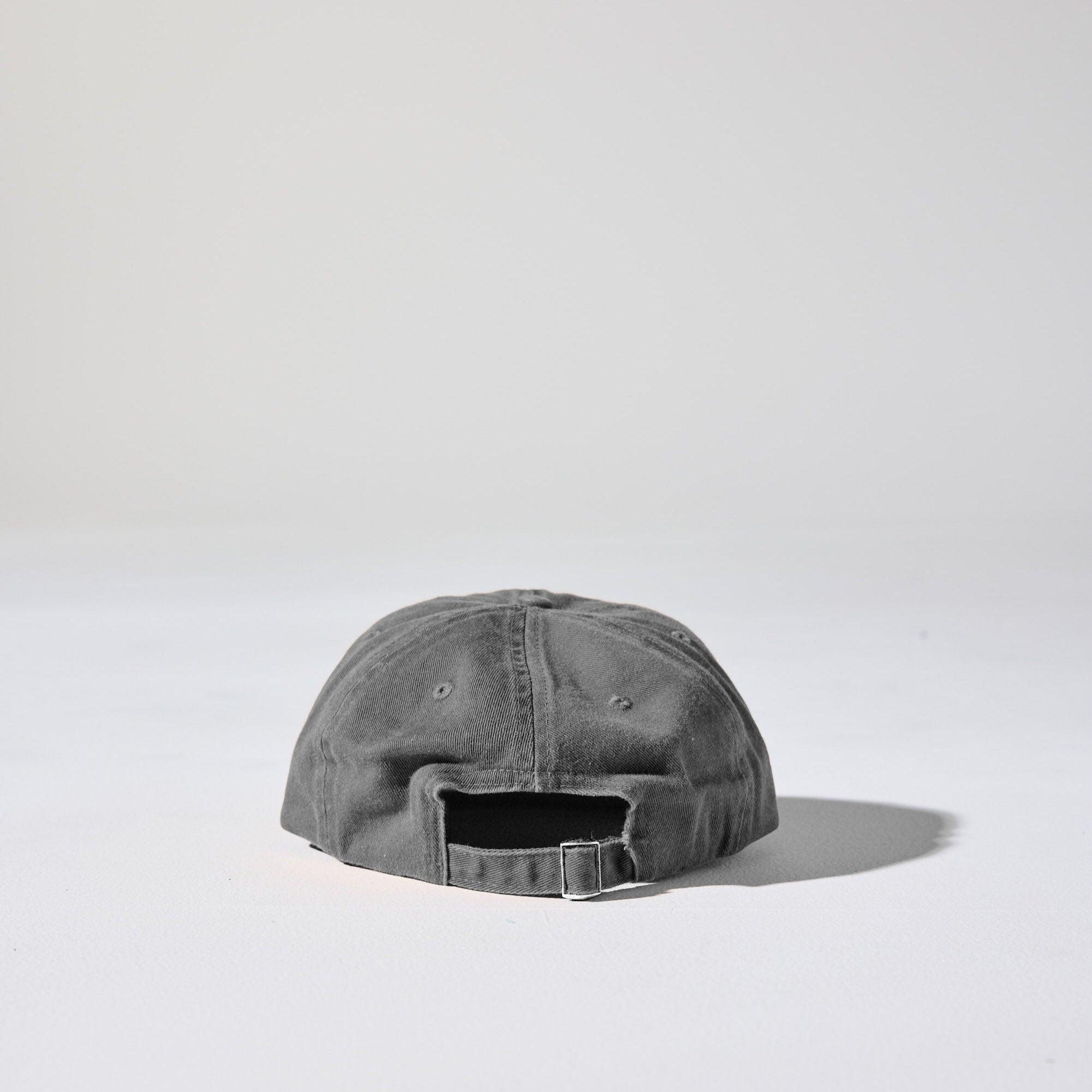 A retro style faded charcoal grey Monday Buckle Cap by House of Peaks with an adjustable strap, placed against a white background.
