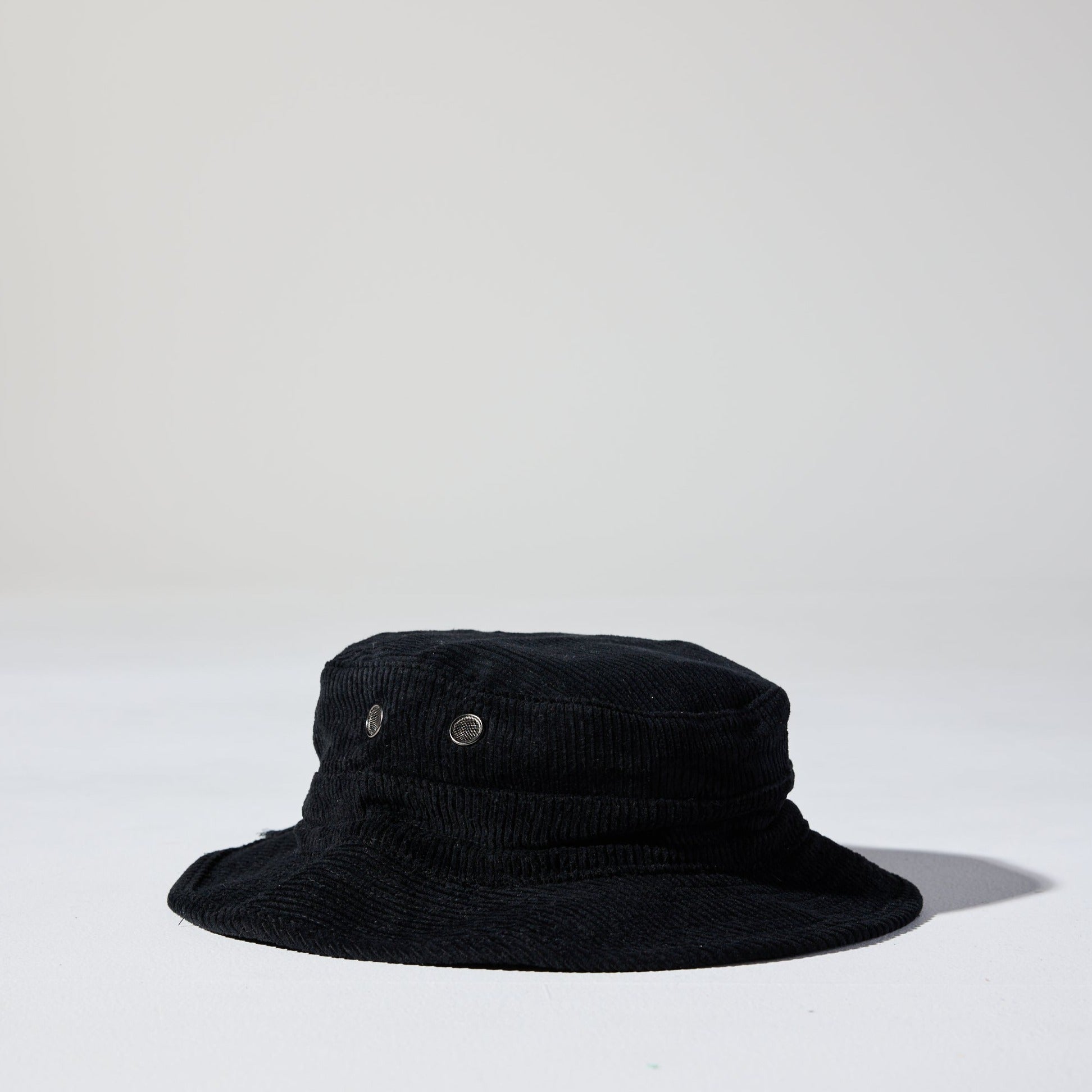 A black Saturday Corduroy Bucket Hat with wide brim, chin strap, and hidden pocket – available in 58cm and 61cm sizes