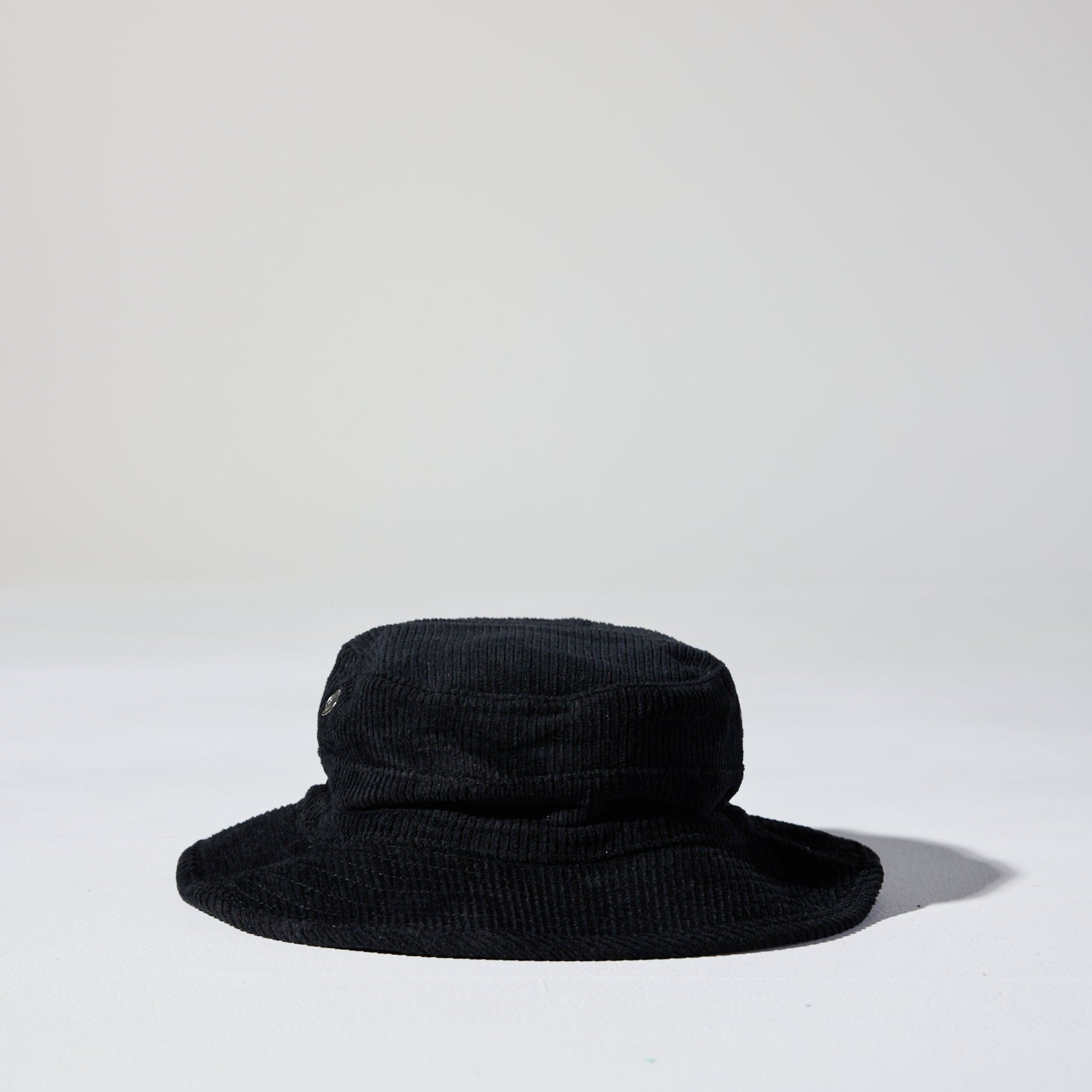 A black Saturday Corduroy Bucket Hat with wide brim, chin strap, and hidden pocket – available in 58cm and 61cm sizes
