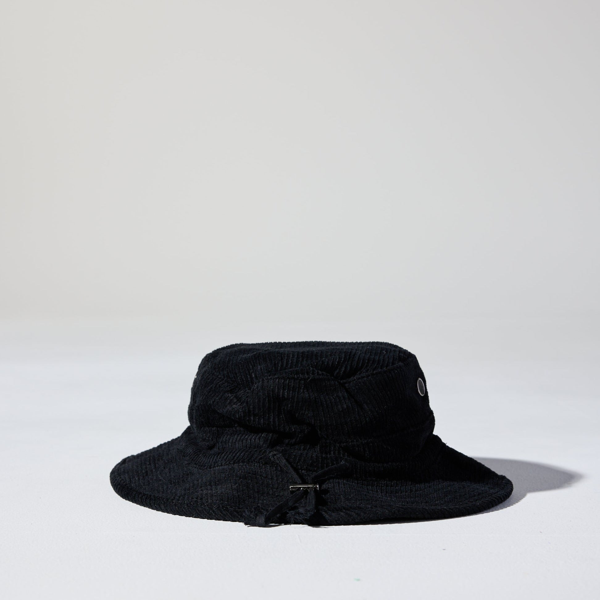 A black Saturday Corduroy Bucket Hat with wide brim, chin strap, and hidden pocket – available in 58cm and 61cm sizes