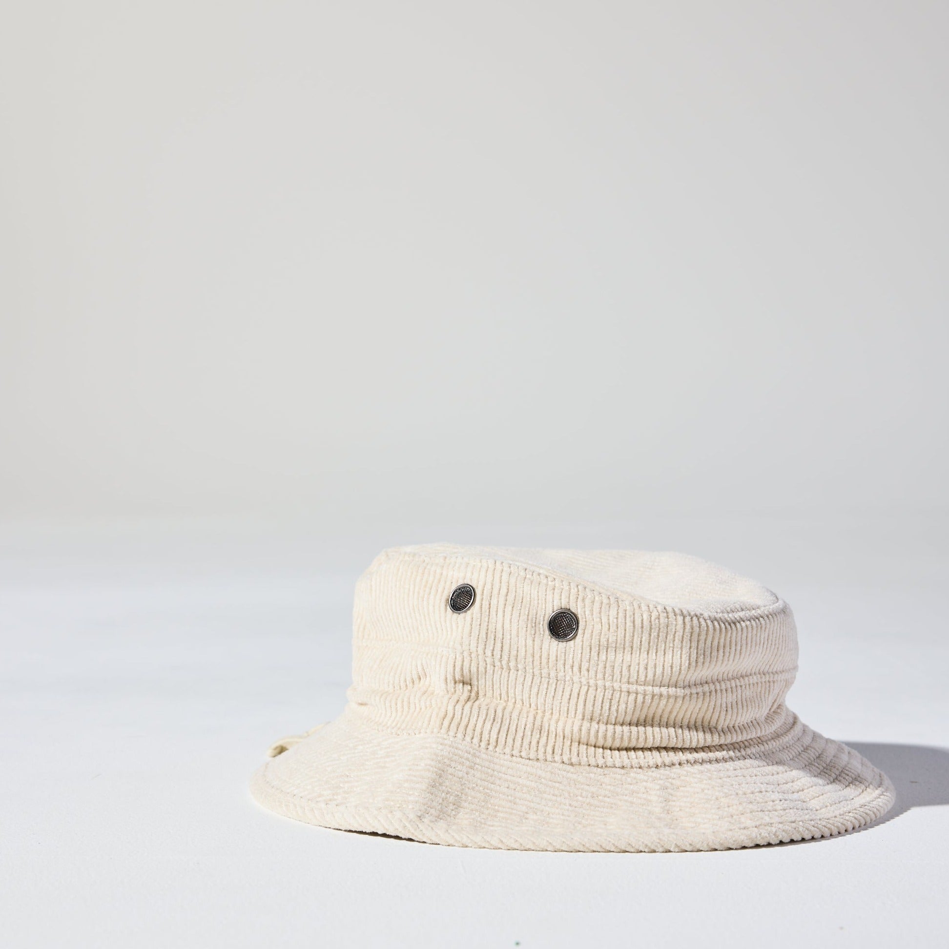 A cream Saturday Corduroy Bucket Hat with wide brim, chin strap, and hidden pocket – available in 58cm and 61cm sizes