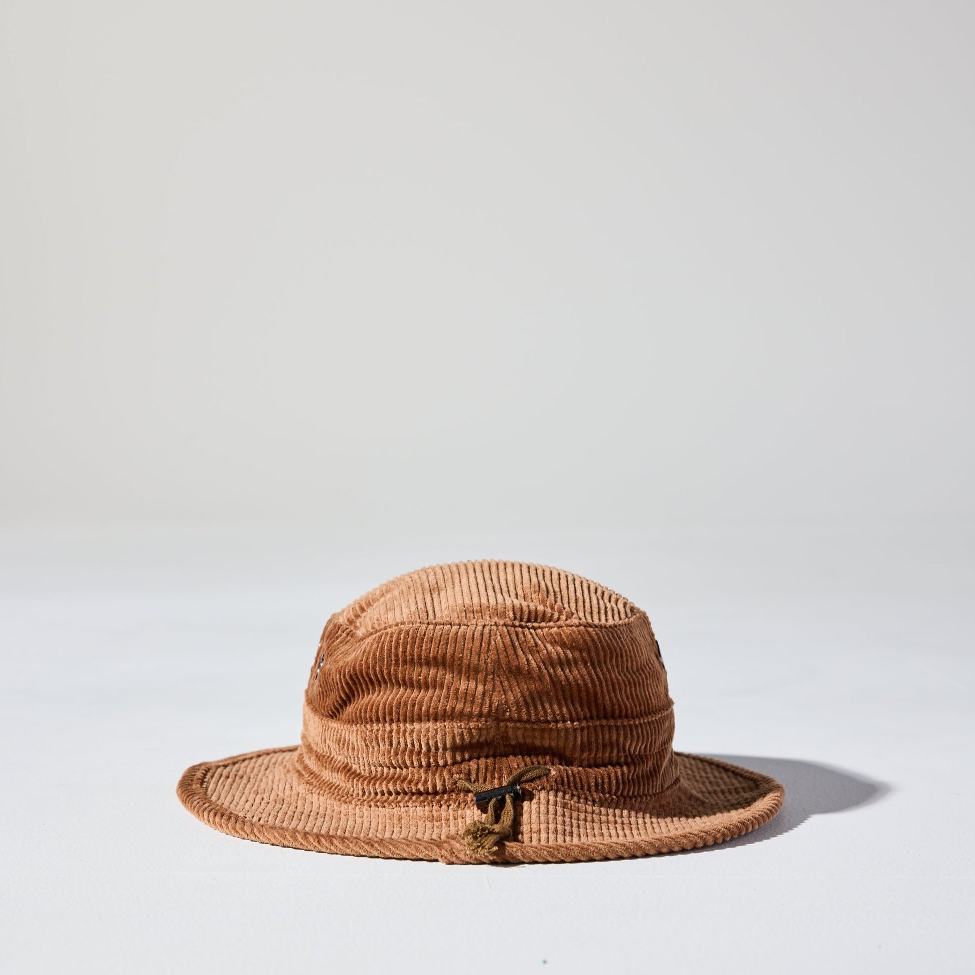 A desert brown Saturday Corduroy Bucket Hat with wide brim, chin strap, and hidden pocket – available in 58cm and 61cm sizes