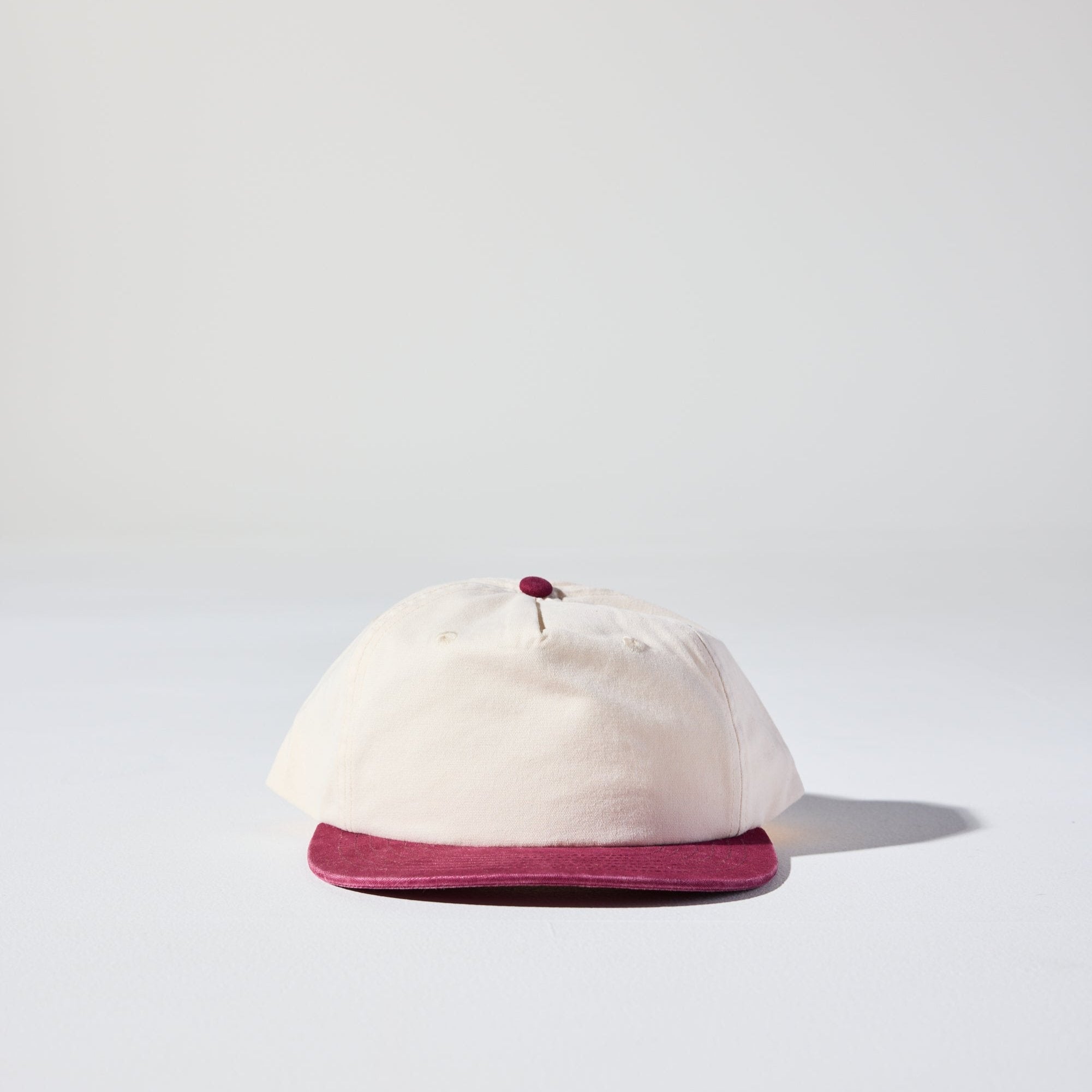 A two-tone cream and burgundy cap with a semi curved peak and adjustable snapback strap.