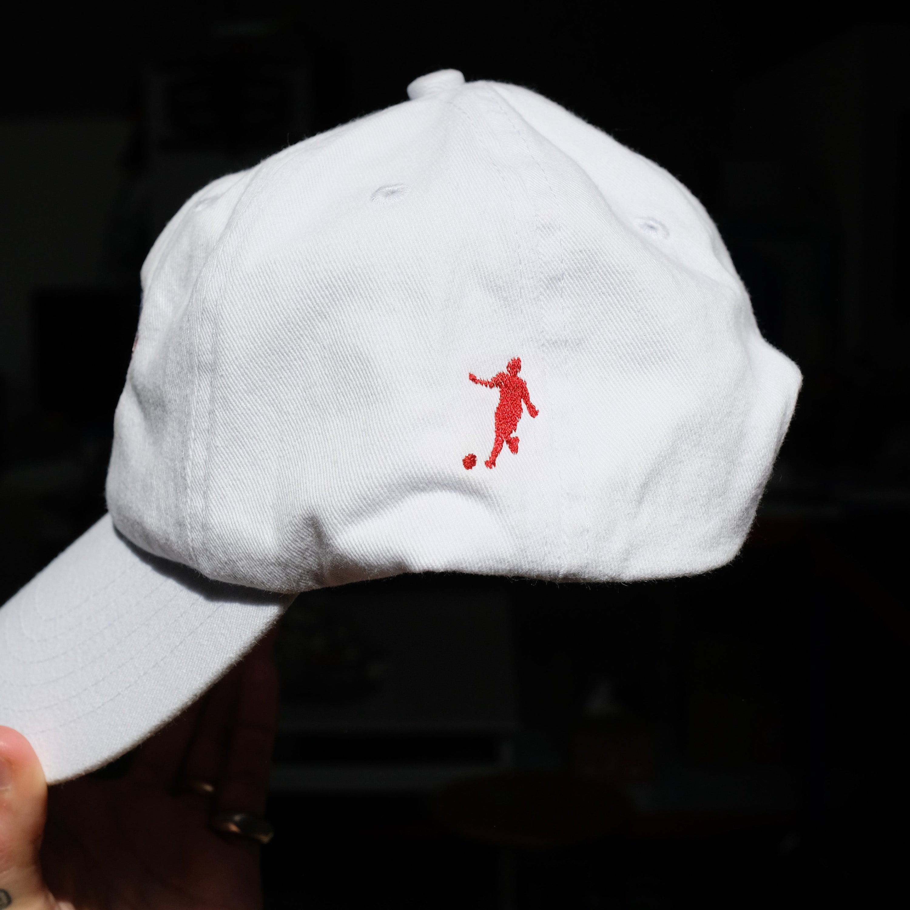 White cap with a red logo held against a dark background